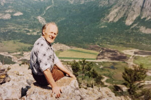 Initiativtakaren: Gudtorm Mikkelson sit i lia på nordsida av Vinddalen. Nede i dalen er det første stykket som er tillaga fôrhausta. På begge sider er det meir under dyrking. Sommaren 1981.